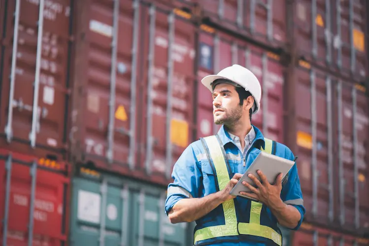 Logistics worker with a tablet in front of stacked shipping containers