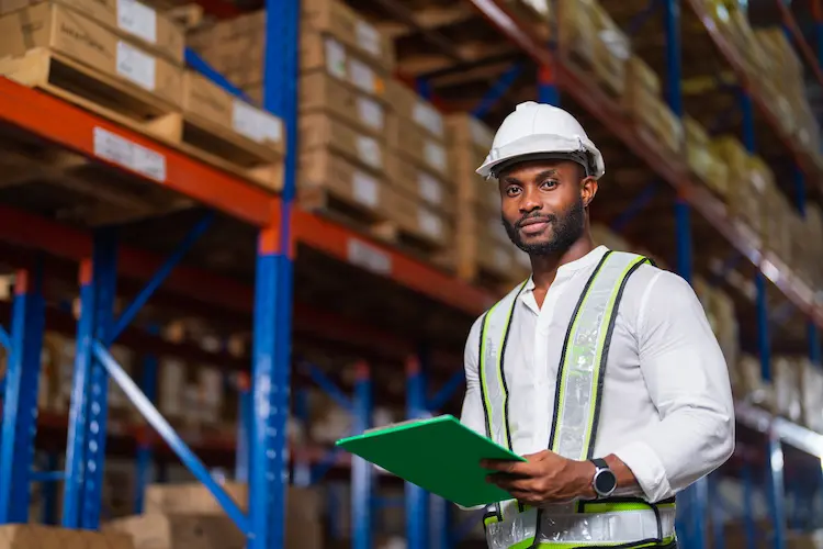 Warehouse manager in a safety vest holding a clipboard in a racking aisle