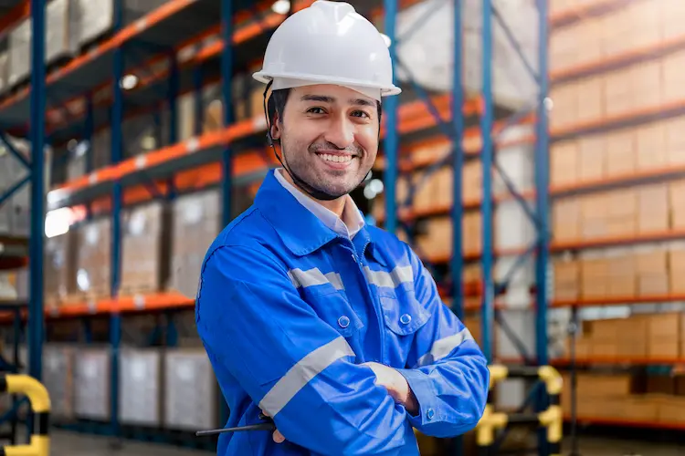 Smiling warehouse worker in a hard hat standing in a racking aisle
