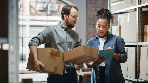 Two colleagues checking a package and clipboard in a stockroom