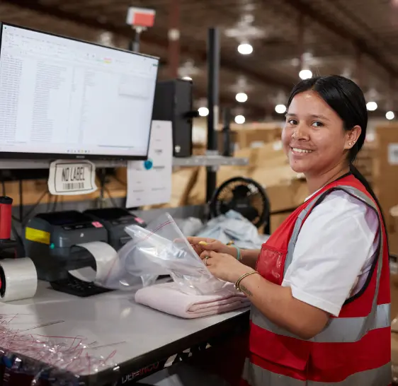 Smiling warehouse associate bagging folded garments at a packing station