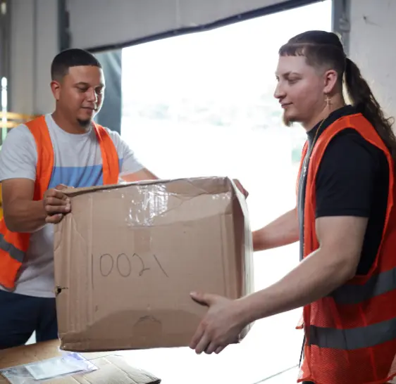 Two warehouse associates passing a box at a loading dock