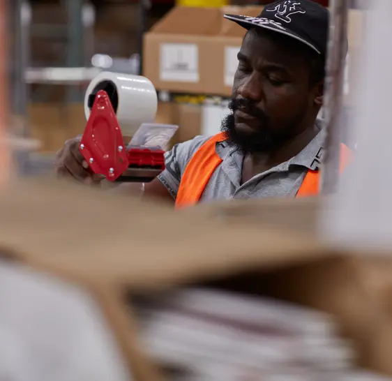 Fulfillment worker sealing a subscription box with packing tape, ensuring secure packaging for kitted orders.