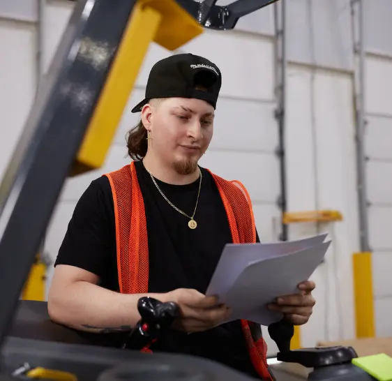 Warehouse associate reviewing paperwork near a forklift