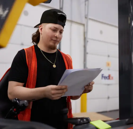 Warehouse associate reviewing paperwork near a forklift