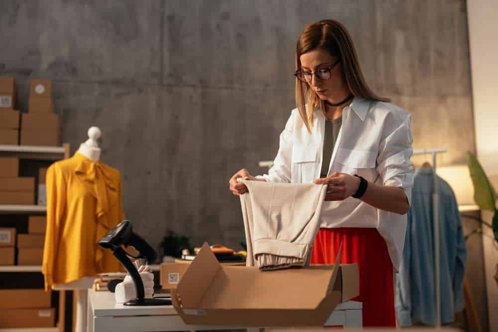 Female business owner examining a white garment for quality before packaging, working in a fashion e-commerce setting