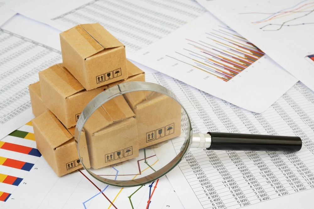 Carton boxes under magnifying glass on financial documents, charts and graphs. Cargo, tariffs and taxes concept
