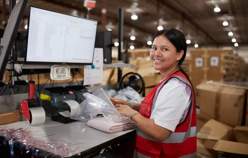 Boxzooka warehouse associate smiling while preparing apparel order for packaging at workstation with Shopify-integrated 3PL software.