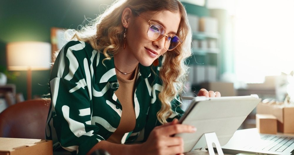 Logistics, online order and tablet with happy woman in office for delivery or shipping schedule. App, supply chain and writing with courier person in depot or warehouse for ecommerce tracking