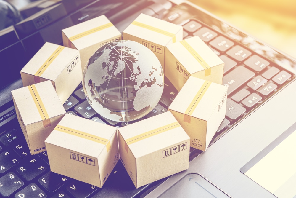 International freight or shipping service for online shopping or ecommerce concept : Paper boxes or carton put in circle around a clear crystal globe with world map on a computer notebook keyboard